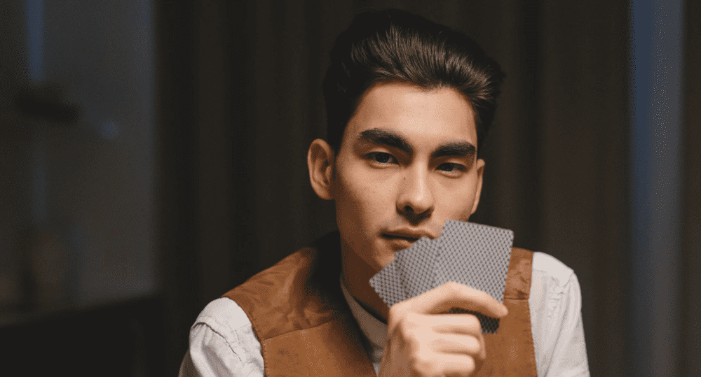 a mysterious man holding poker cards in front of his face